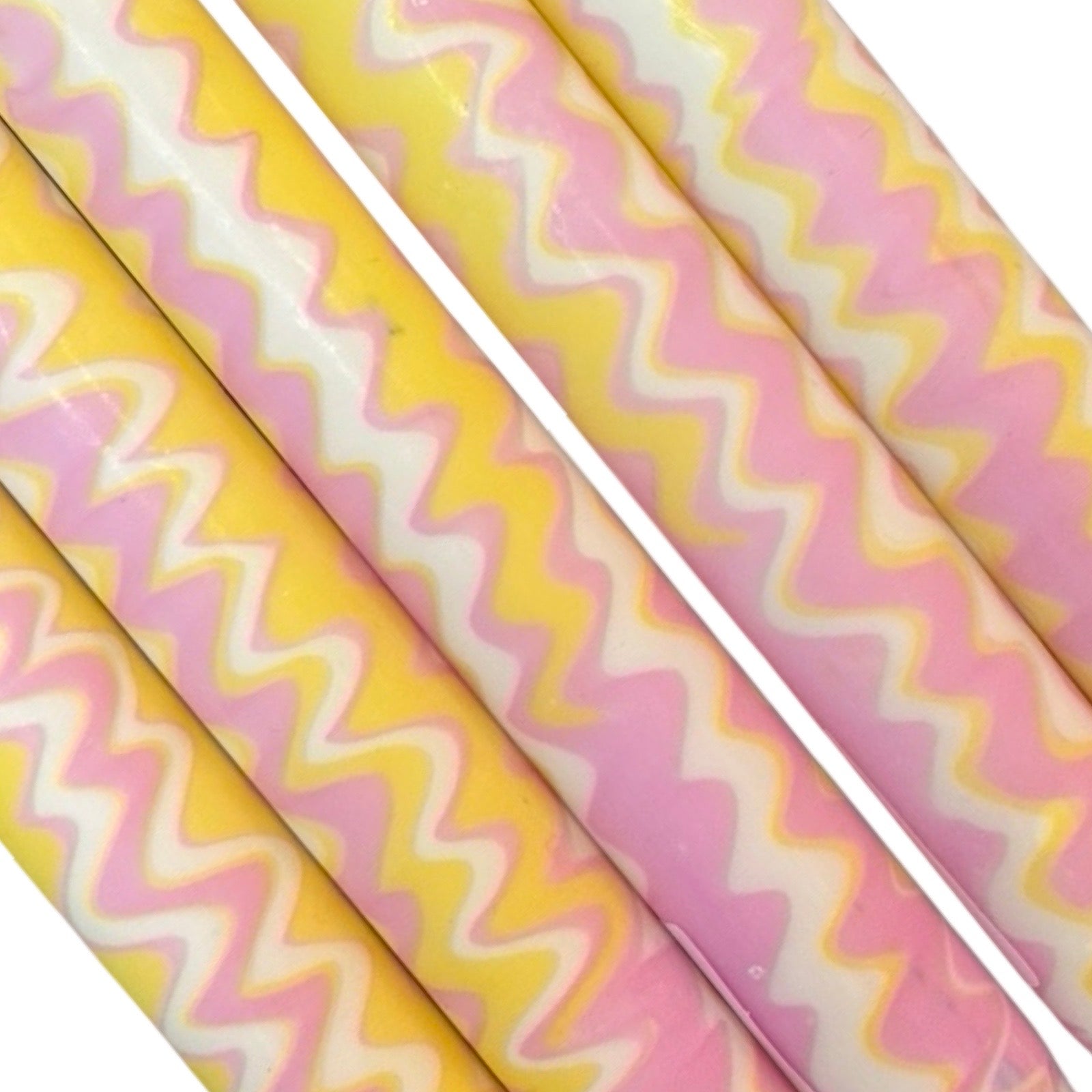 A row of 5 handmade dinner candle marbled in a yellow and pink zig zag pattern on a white background.