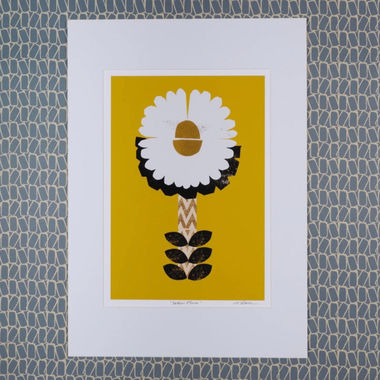 Framed artwork of a stylised flower on a yellow background, mounted on a textured blue wall.