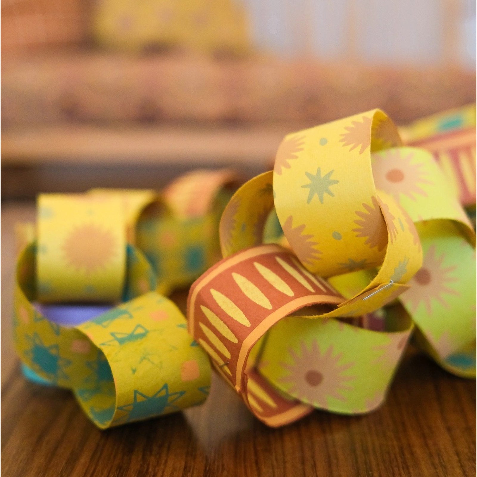 A paper chain made from yellow paper with pink stars, yellow paper with green stars and brown paper with yellow ovals.