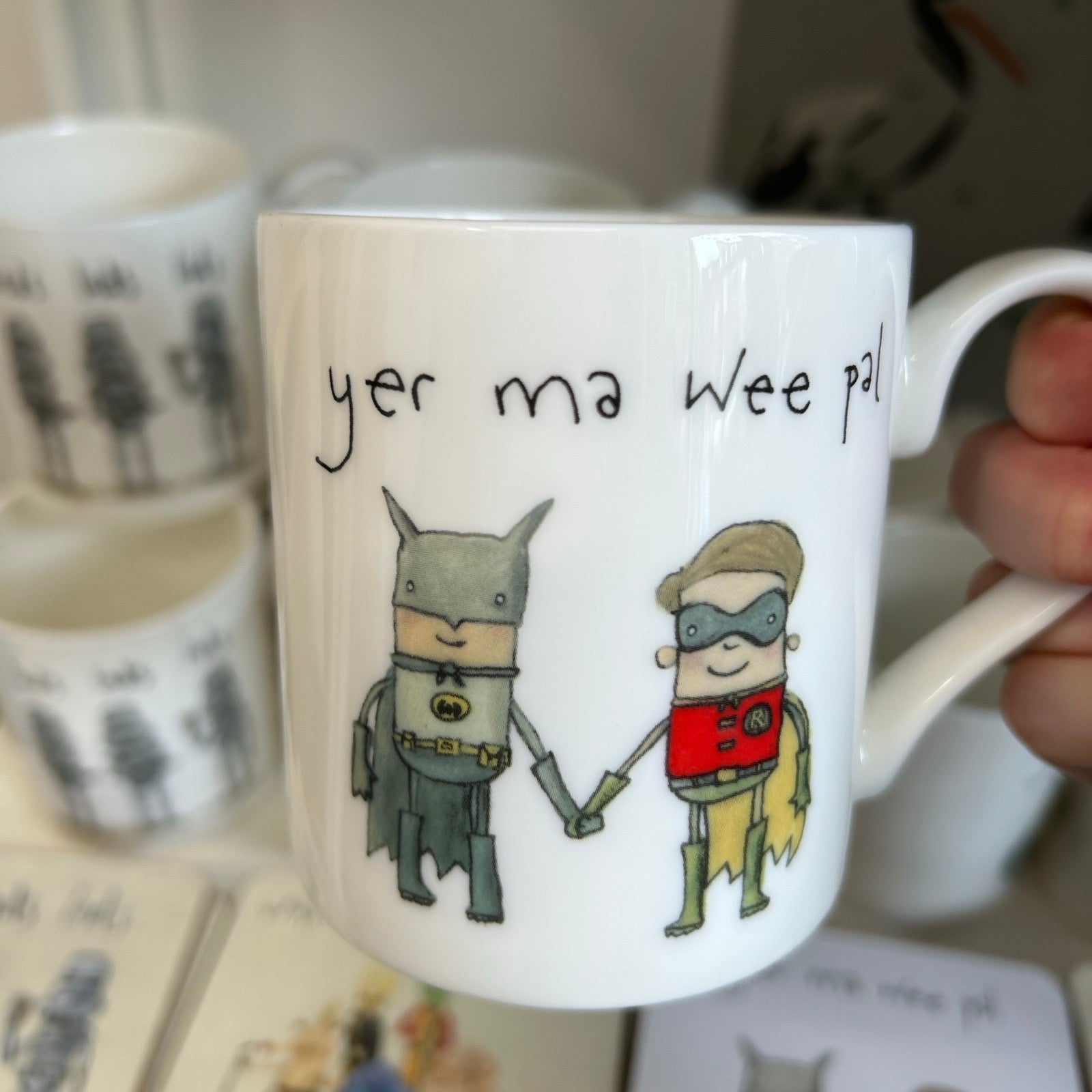 Mug with cartoon characters holding hands and text 'yer ma wee pal' on a blurred background.