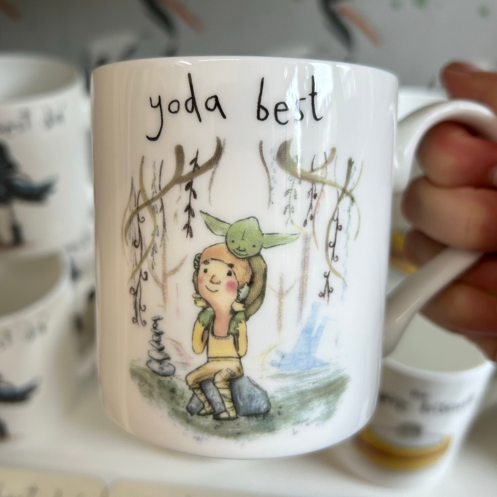Mug with illustration of a Luke Skywalker and Yoda, and text 'yoda best', held by a hand.