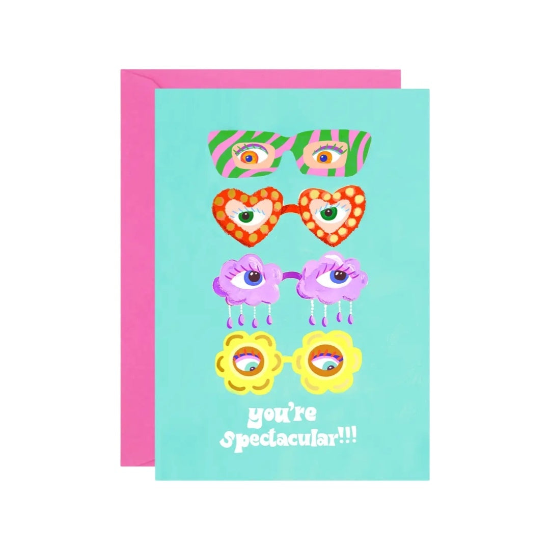 Card featuring 4 pairs of retro-style eyeglasses, one green and pink striped, one red in the shape of love hearts, one purple in the shape of clouds and one yellow in the shape of flowers. The text 'you're spectacular' is written underneath in white text, all on a turquoise background.