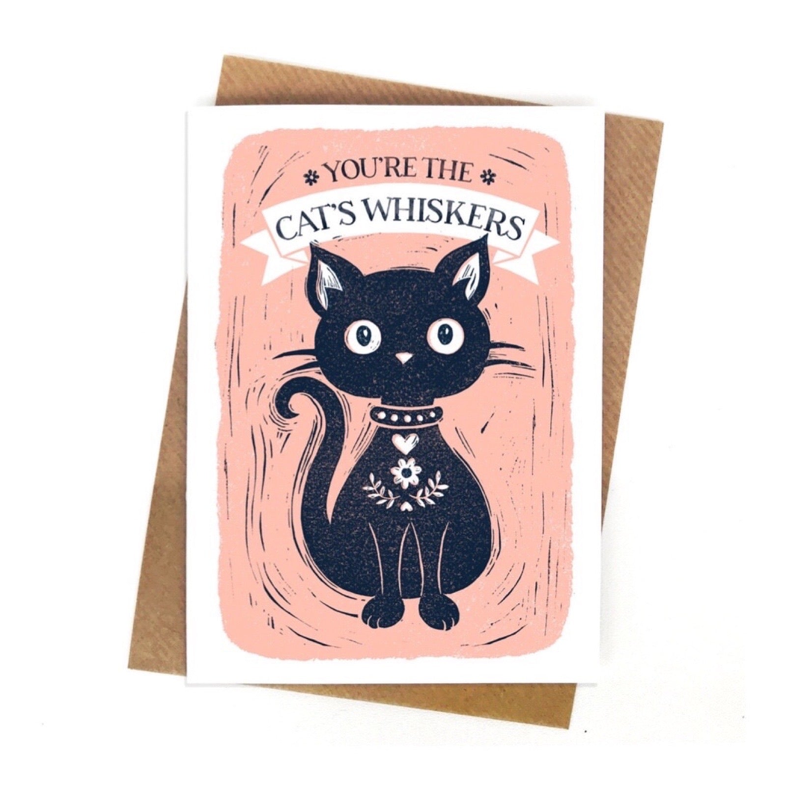 Greeting card with a black cat illustration and text on a pink background, with a brown envelope on a white background.