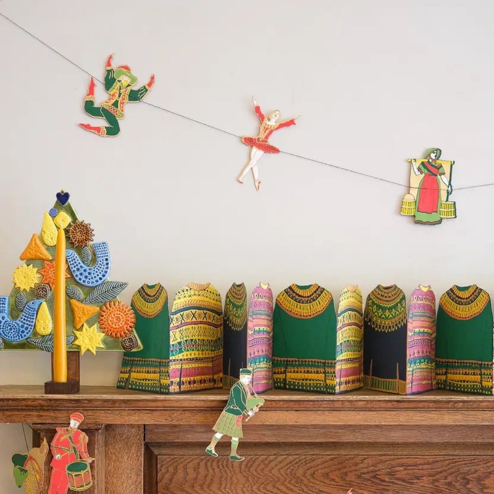 Hanging 12 days of Christmas paper garland, featuring twelve screen-printed characters including a piper, a dancer and a drummer drumming.
