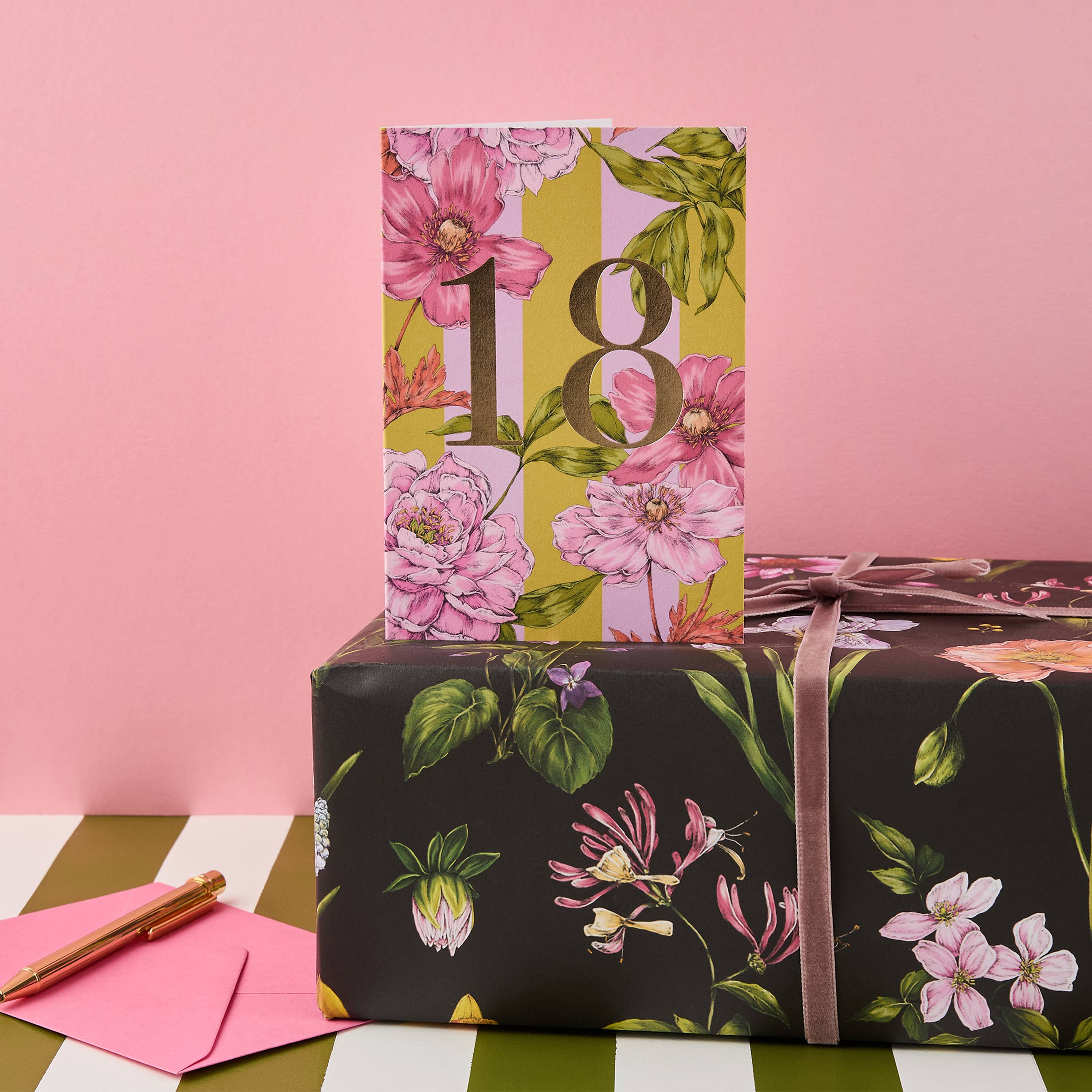 Gift box with floral wrapping paper and a pink ribbon on a pink background.