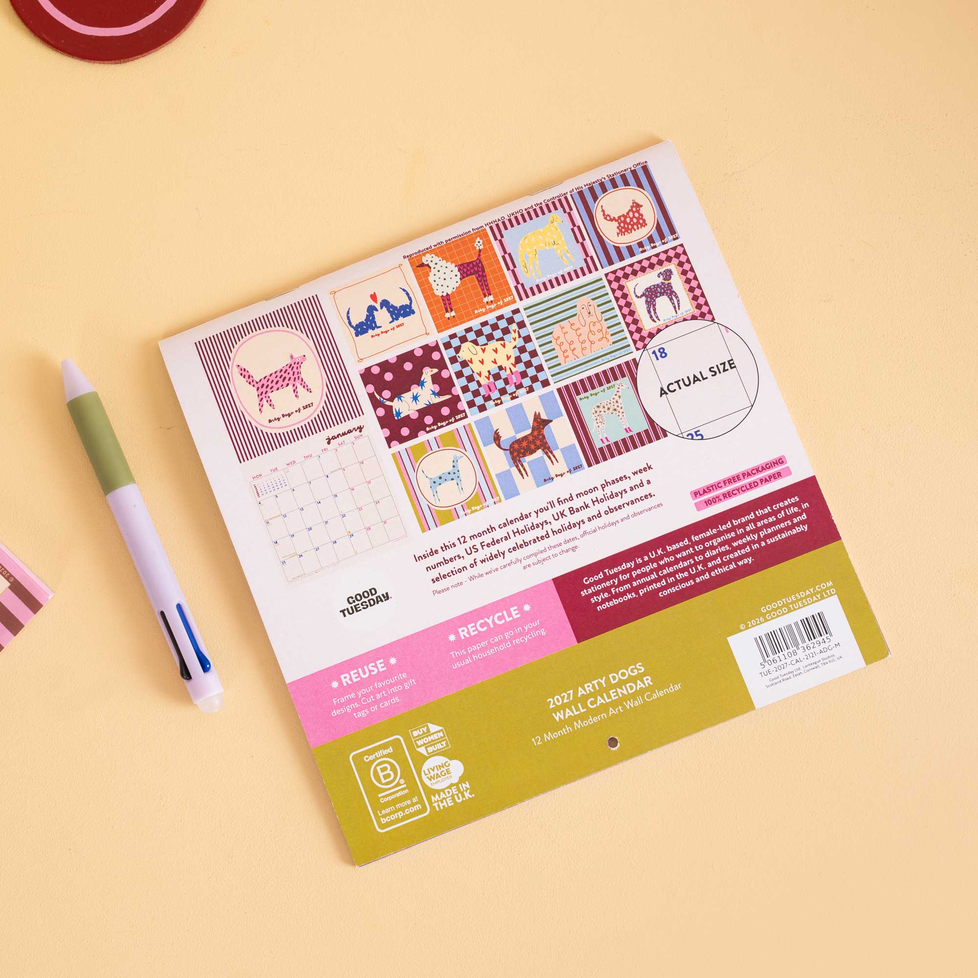 A reusable 2027 dog walk calendar sticker pack by Good Paper, displayed on a light beige background with a green and white pen nearby. The back of the pack features colorful patchwork dog illustrations and product details.