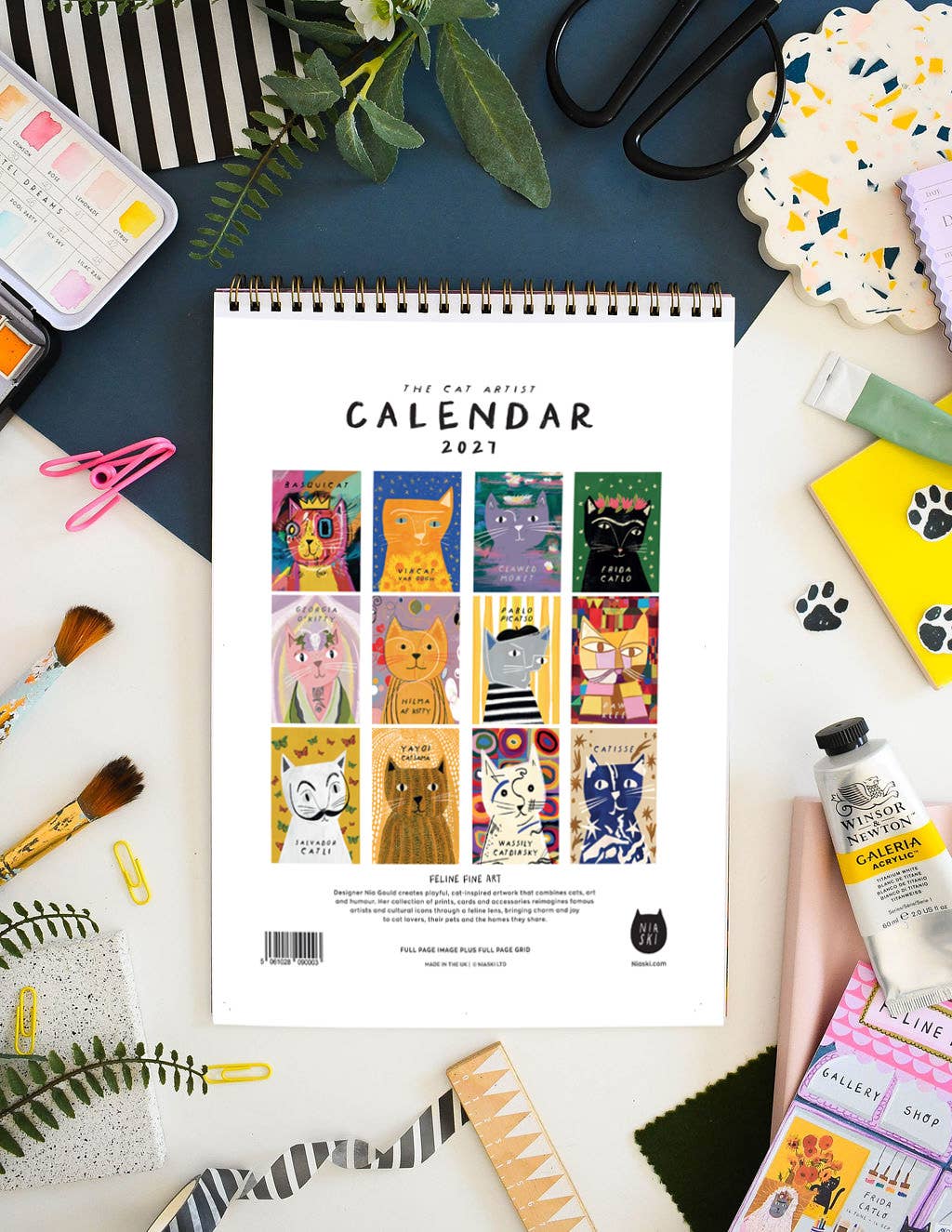A spiral-bound 2027 calendar titled 'The Cat Artist' on a white and blue surface. The calendar cover features a grid of colourful cartoon cat illustrations.
