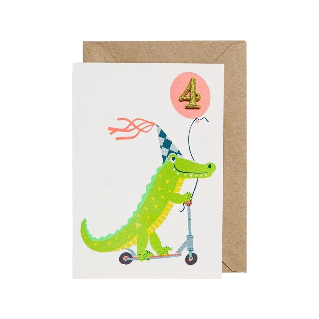 4th birthday card featuring a crocodile wearing a party hat on a scooter and '4' in a pink balloon.