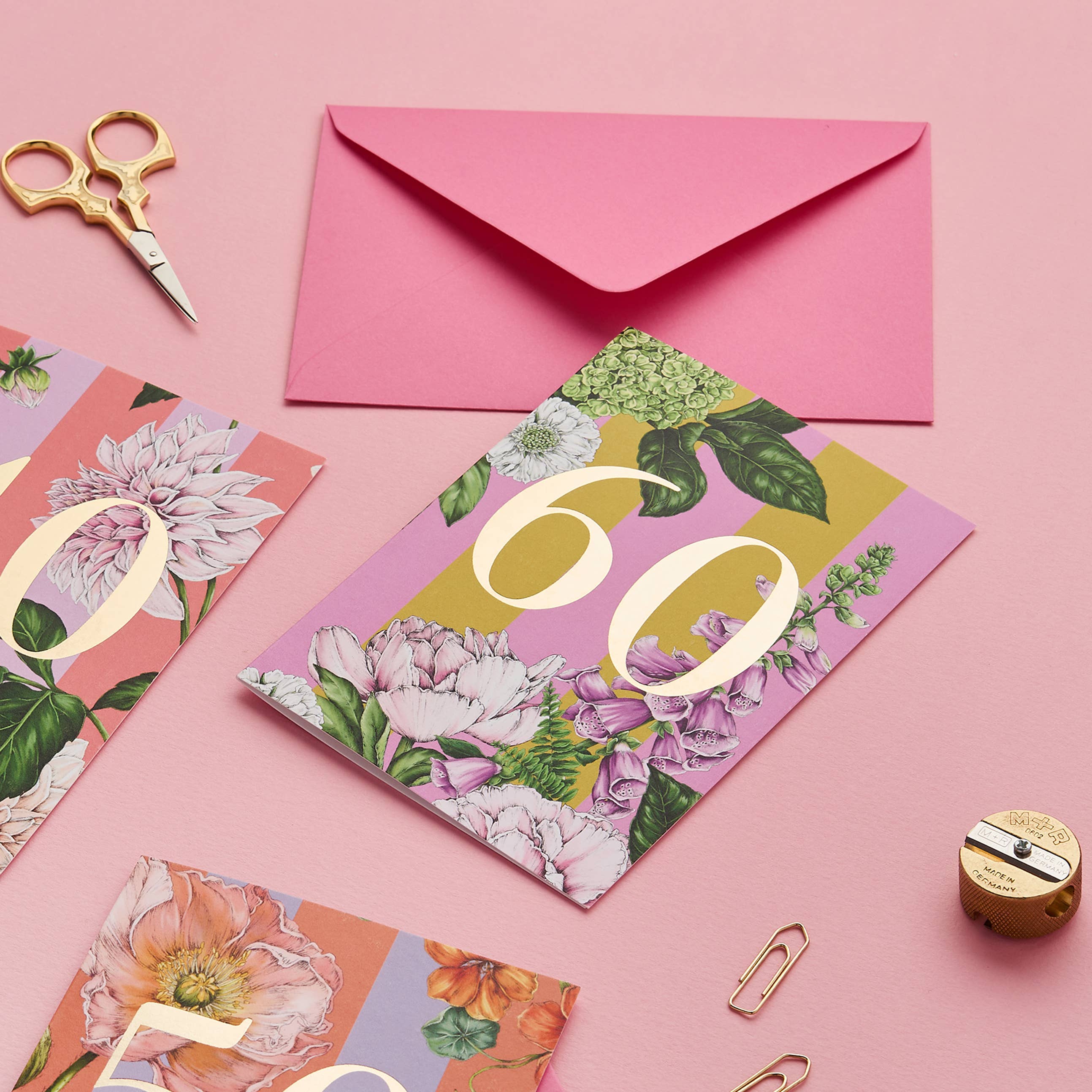 Floral birthday card with number 60 on a pink background with envelope and stationery items.