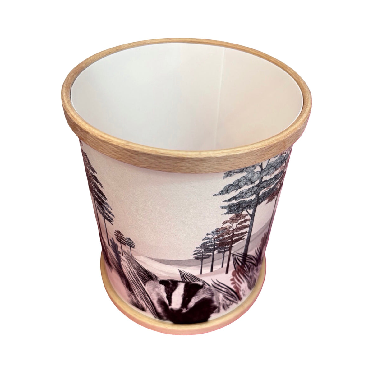 A cylindrical candle holder with a light wood rim and base, featuring an illustration of a badger among trees and reeds.