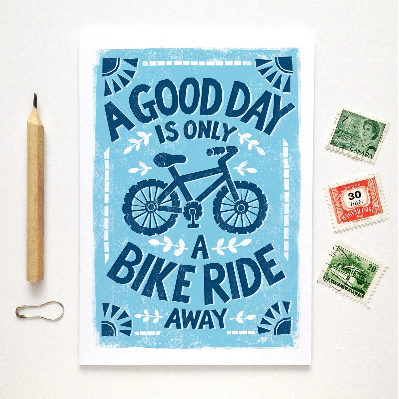 Poster with bicycle design and text 'A good day is only a bike ride away' on a white background with stationery items.