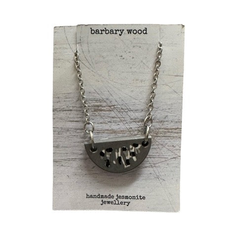 A grey half moon necklace with a black and white abstract design on a silver chain