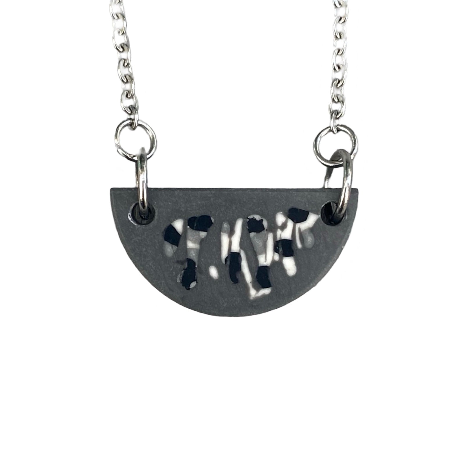 A grey half moon necklace with a black and white abstract design on a silver chain