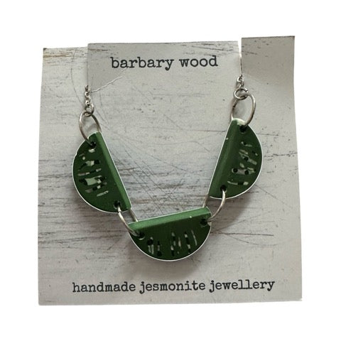 A necklace with three half-moon resin shapes in green with a black and white abstract pattern held together with silver findings on a silver chain.