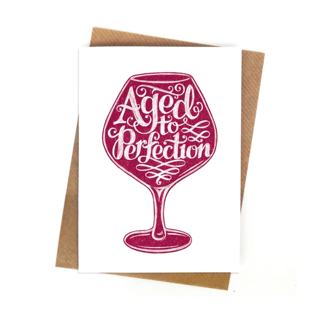 A white birthday card with a red wine glass and the text 'aged to perfection' inside the glass.