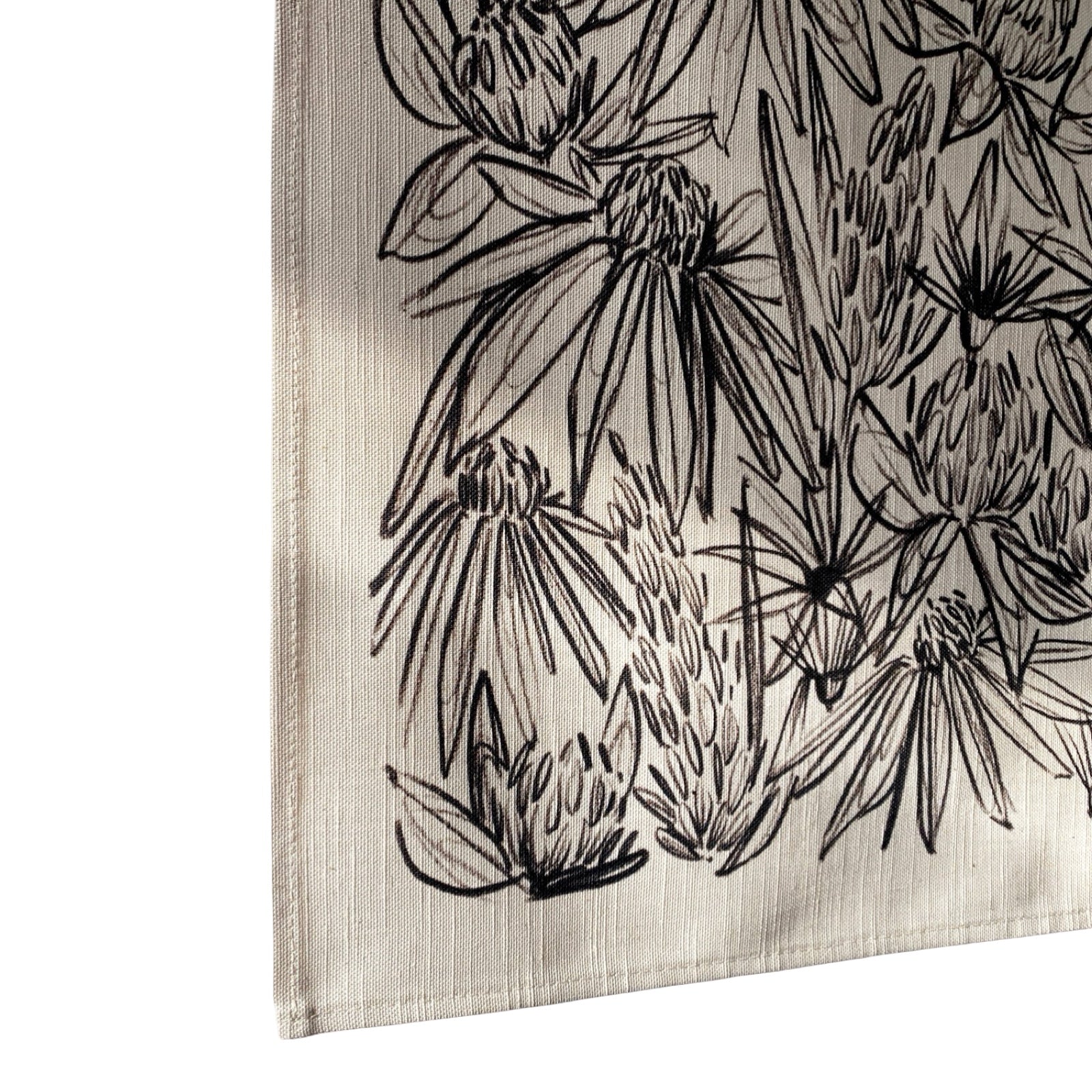 Cream coloured fabric with a black ink floral design hanging on a white wall.