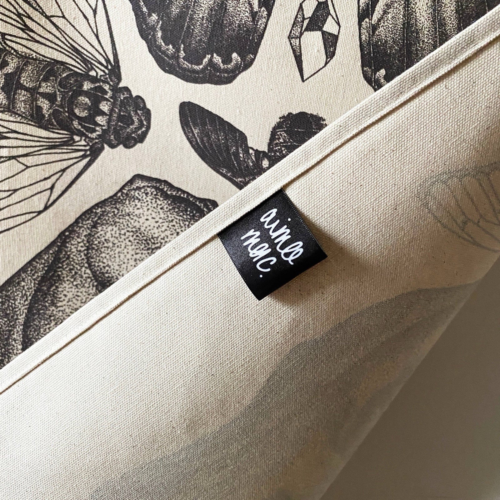 Cream coloured fabric with a black ink design, a folded stitched seam and a black Aimee Mac label.