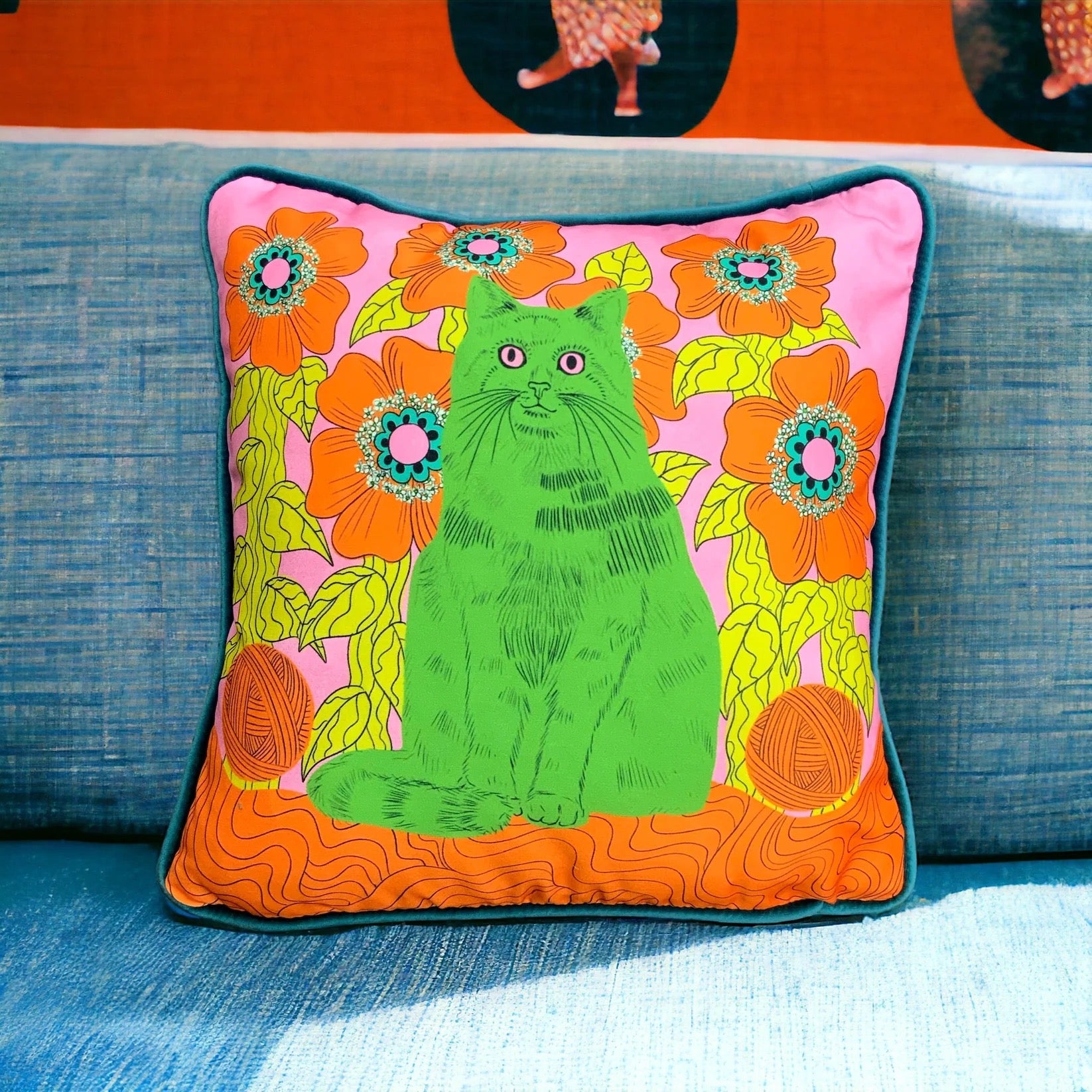 Colourful cushion with a green cat and orange flowers on a blue couch.