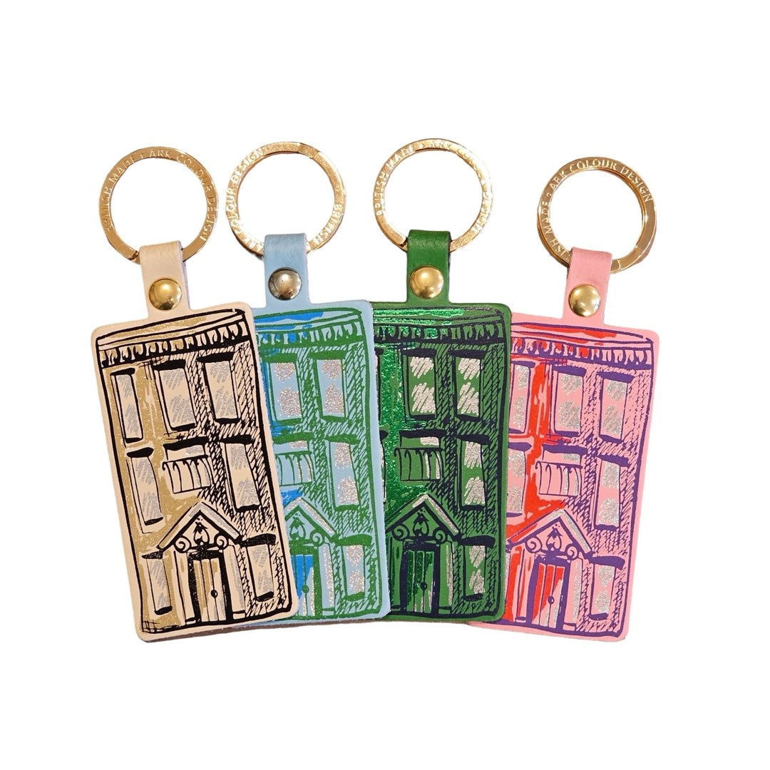 4 rectangular leather keyrings with an illustration of an apartment block on them and a gold-coloured keyring. From left to right cream, blue, green and pink.