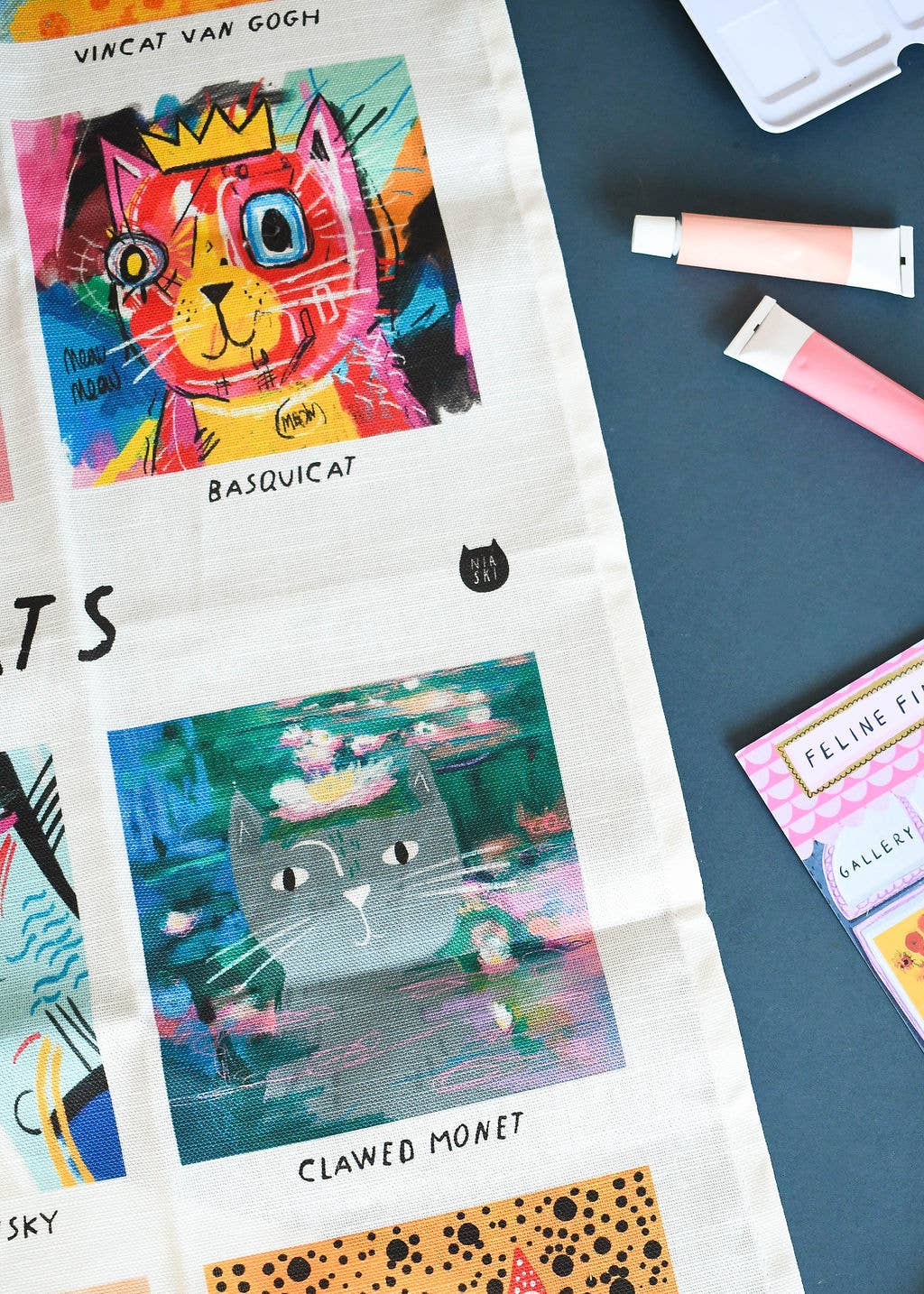 Colourful cat illustrations on a fabric with art supplies in the background.