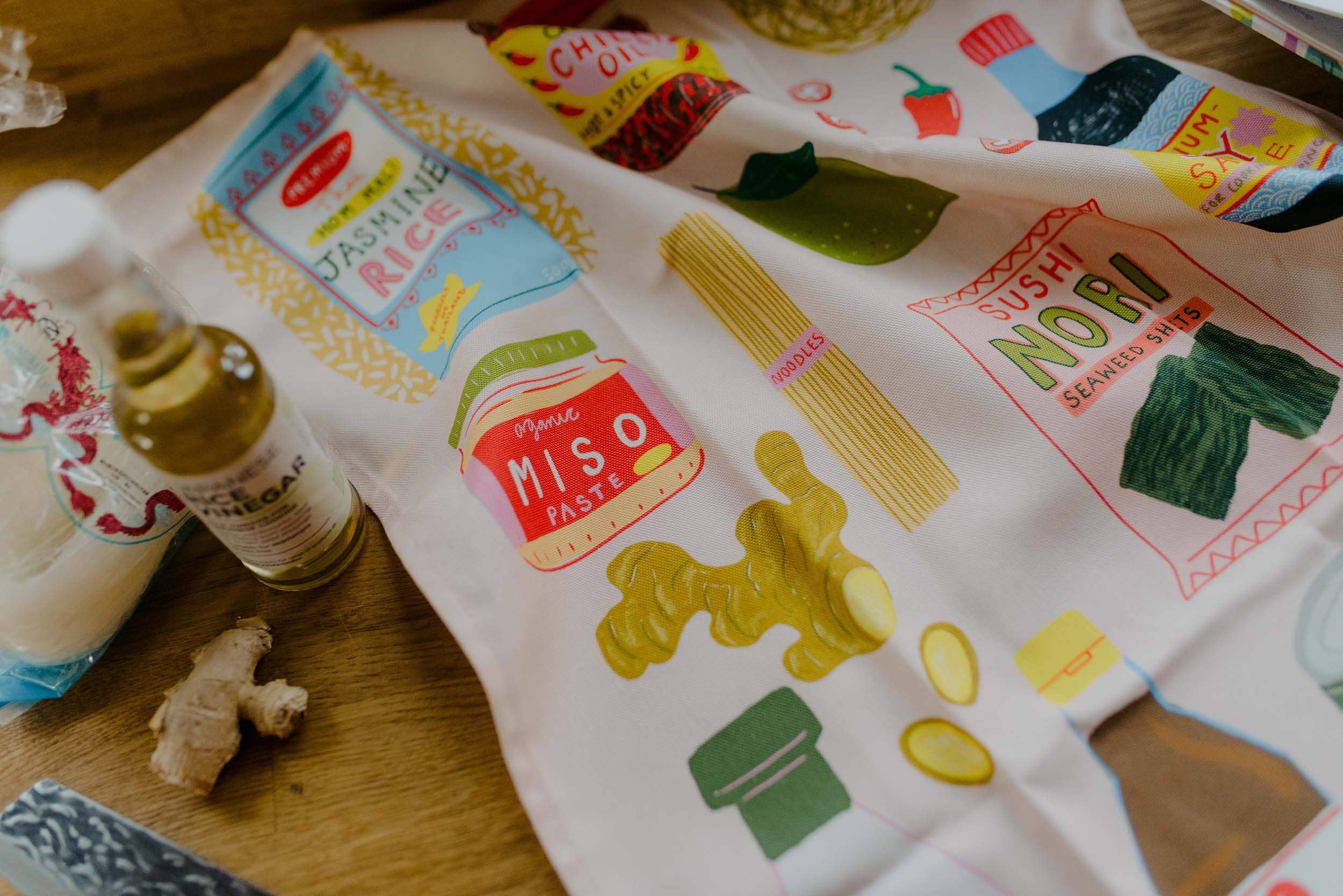 Tea towel with food-themed designs and text on a wooden surface.