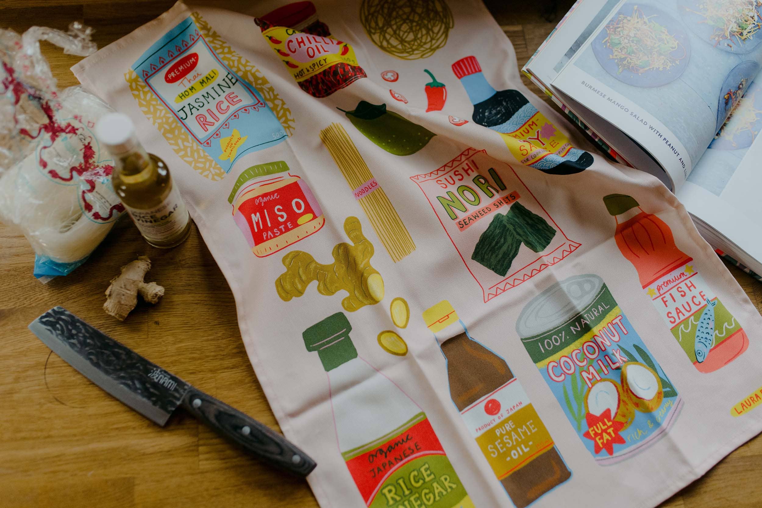 Fabric tea towel with food-themed designs on a wooden surface.
