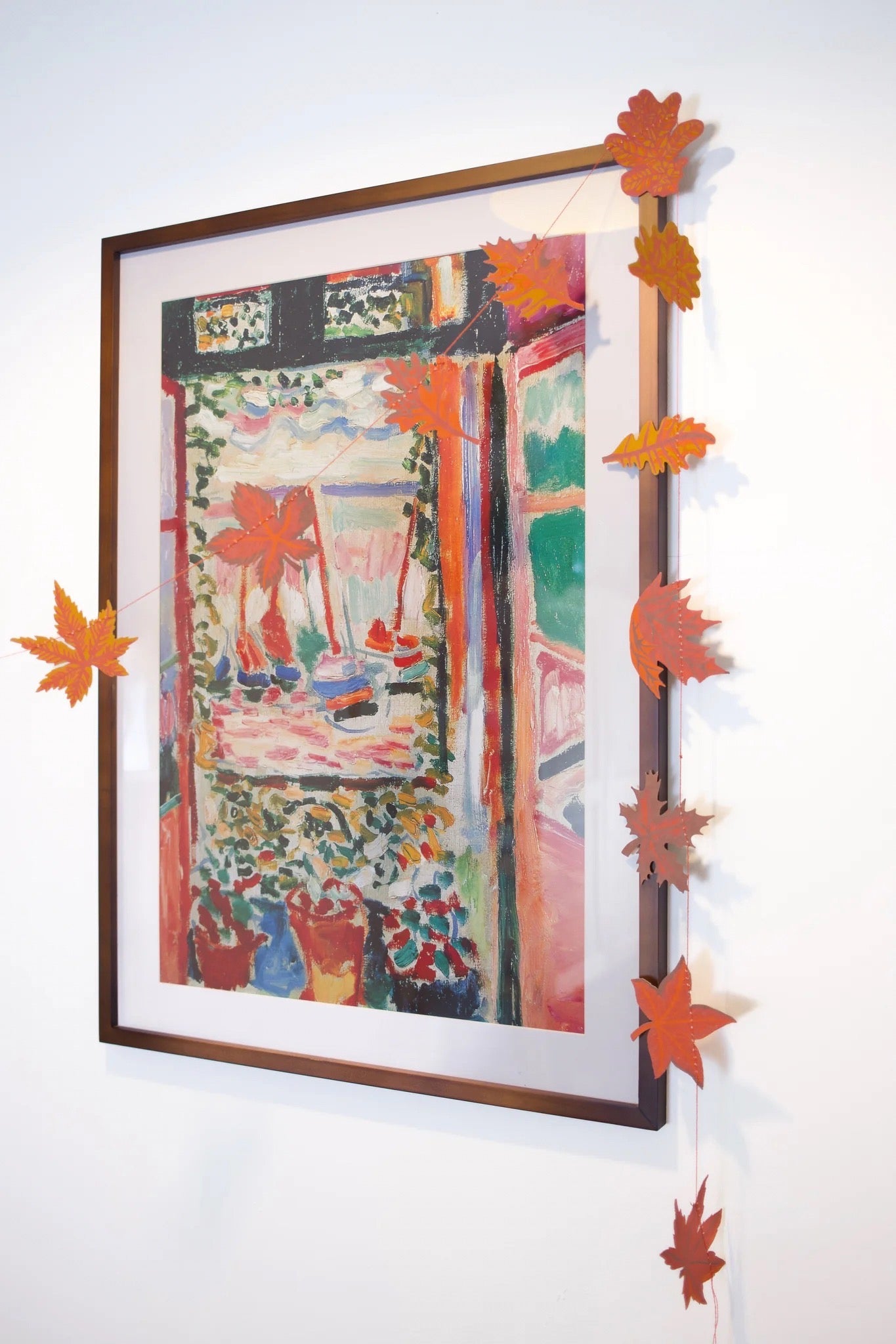 Framed artwork with colourful abstract design on a white wall, decorated with orange paper leaves.