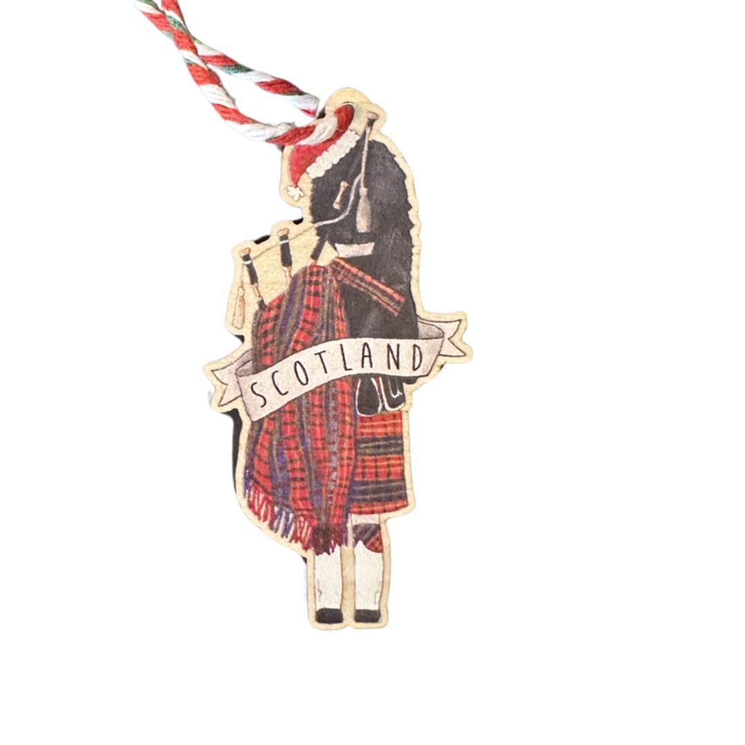 A wooden Christmas decoration of a Scottish bagpiper wearing a santa hat.