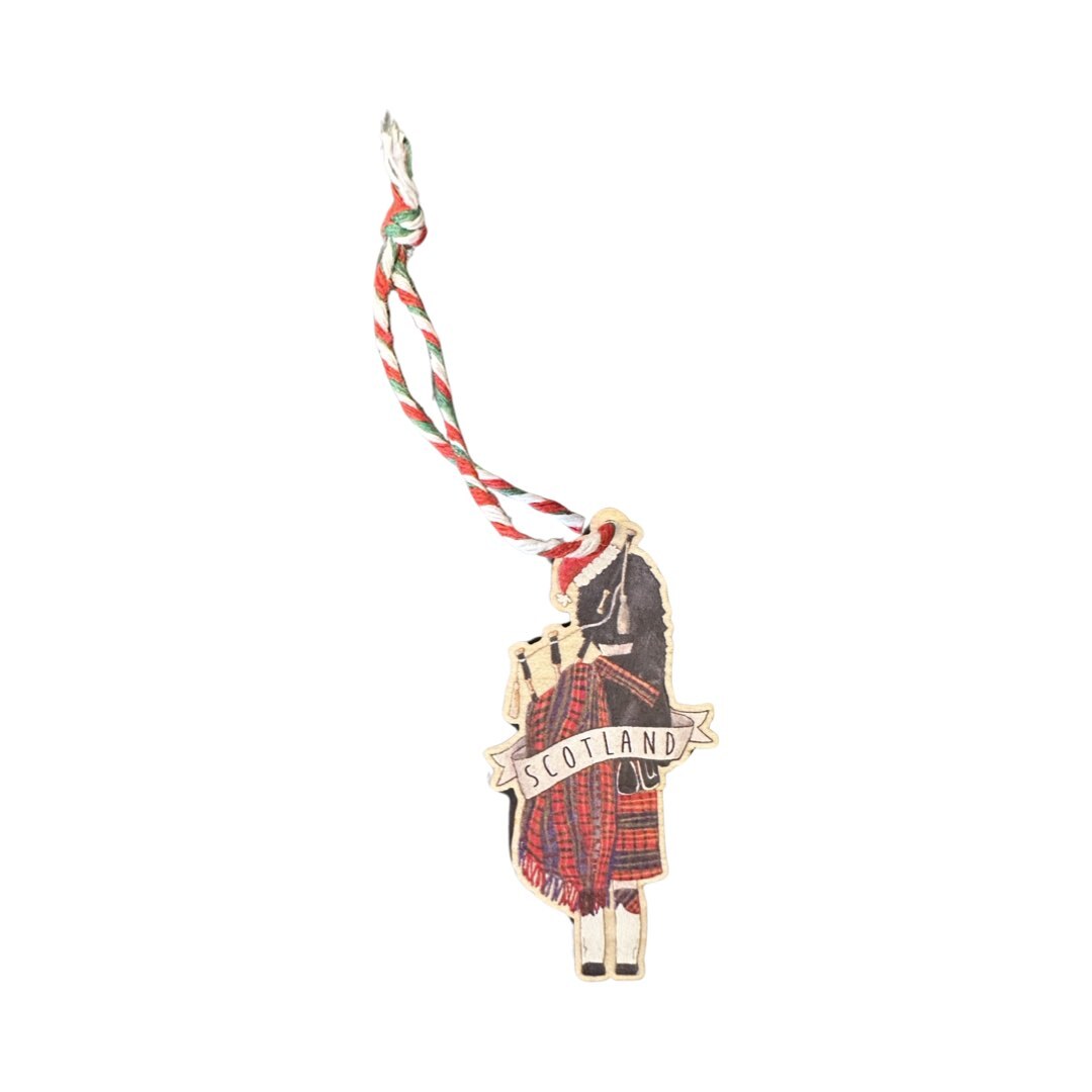 A wooden Christmas decoration of a Scottish bagpiper wearing a santa hat.
