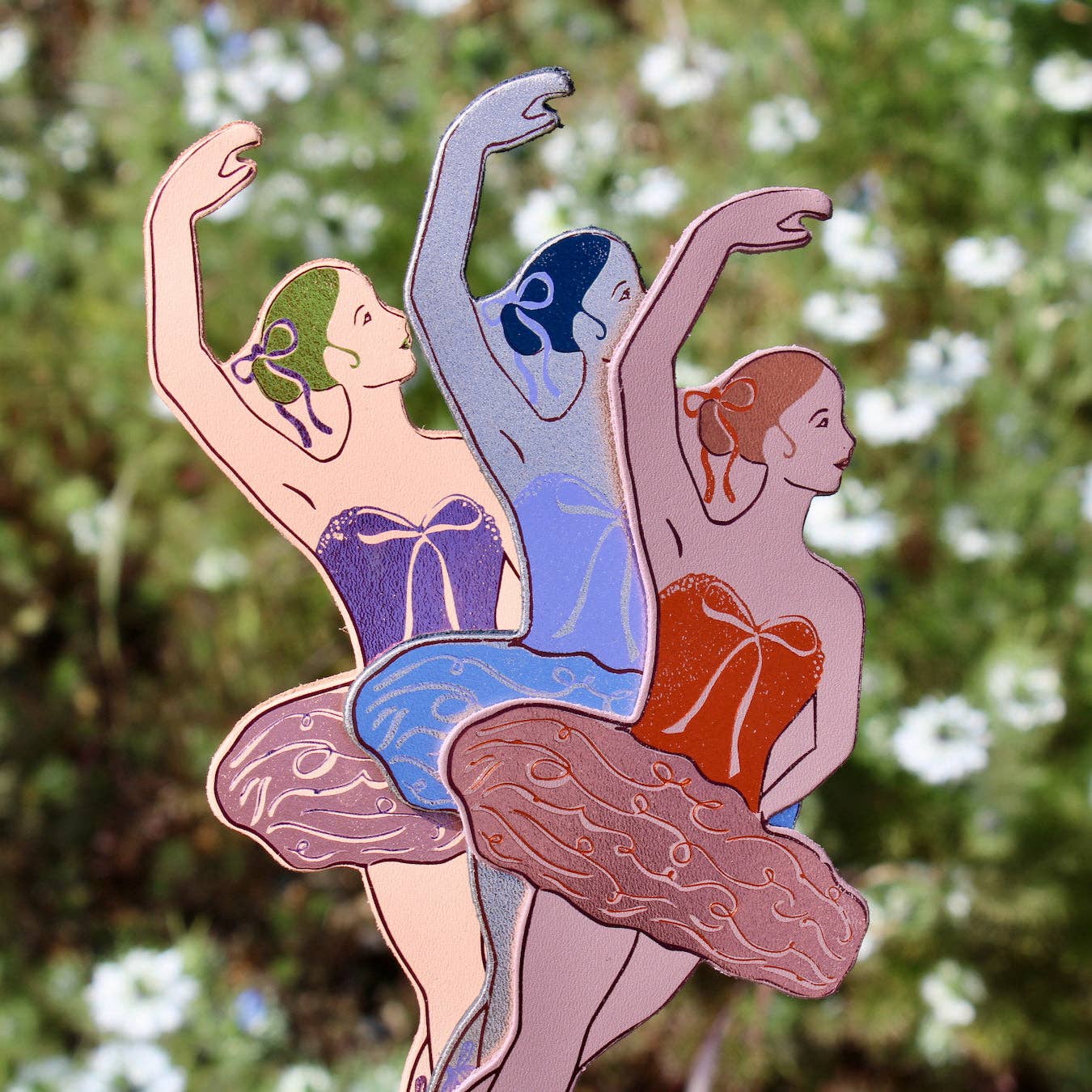 Three stylised figures in ballet poses against a blurred trees background.