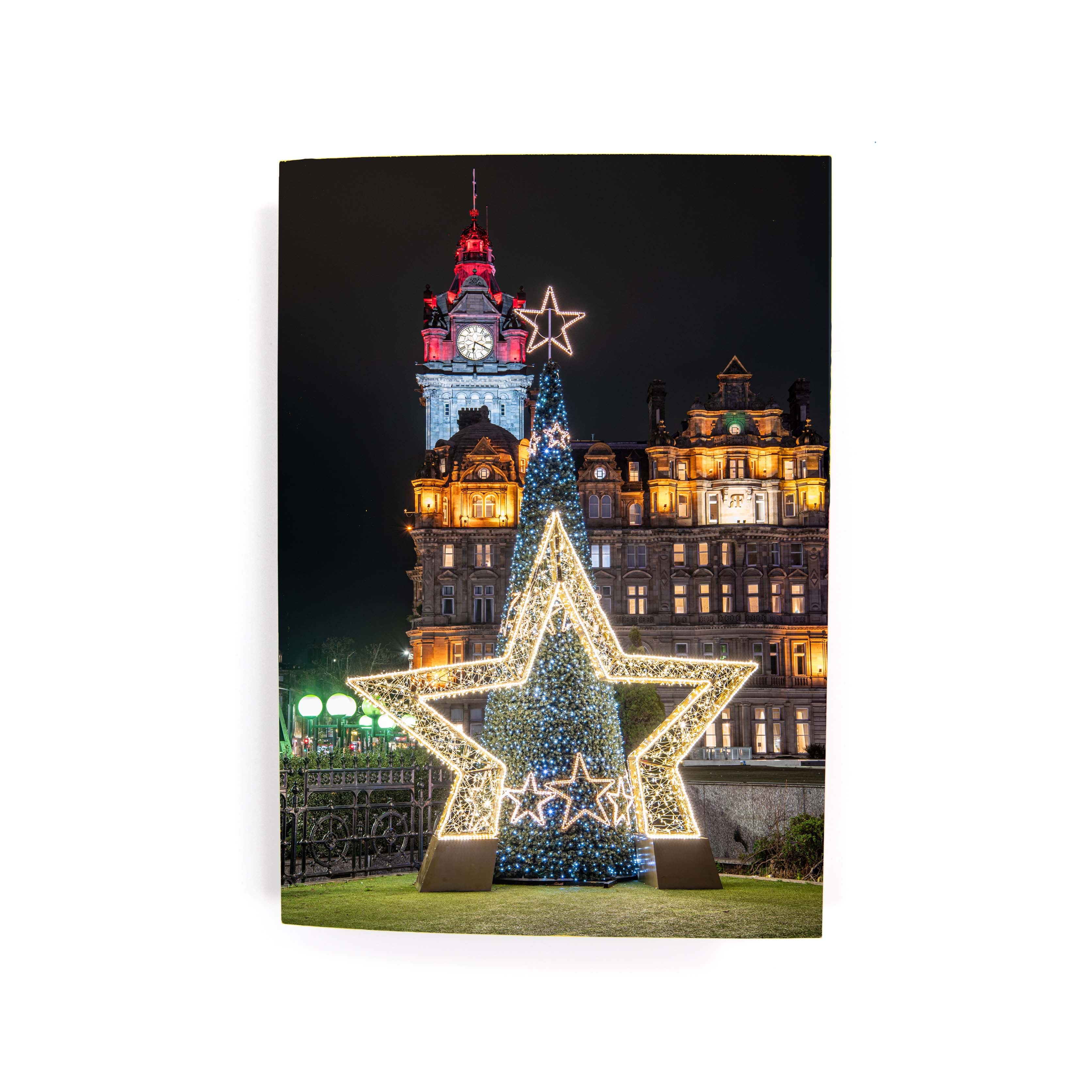 Decorative star and Christmas tree in front of a building with festive lights at night.