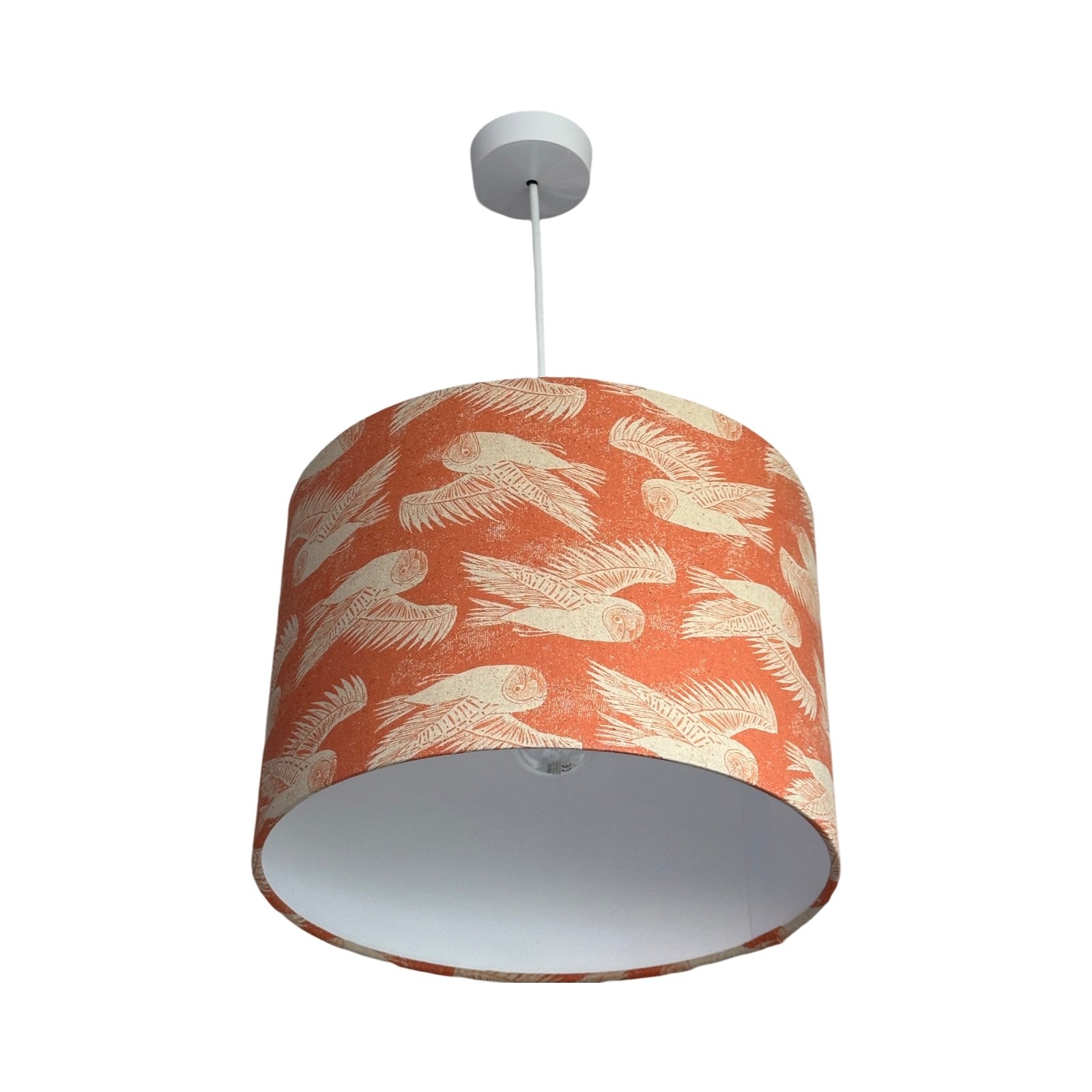 Drum lampshade covered in coral fabric with cream flying barn owls hanging in room with cream walls