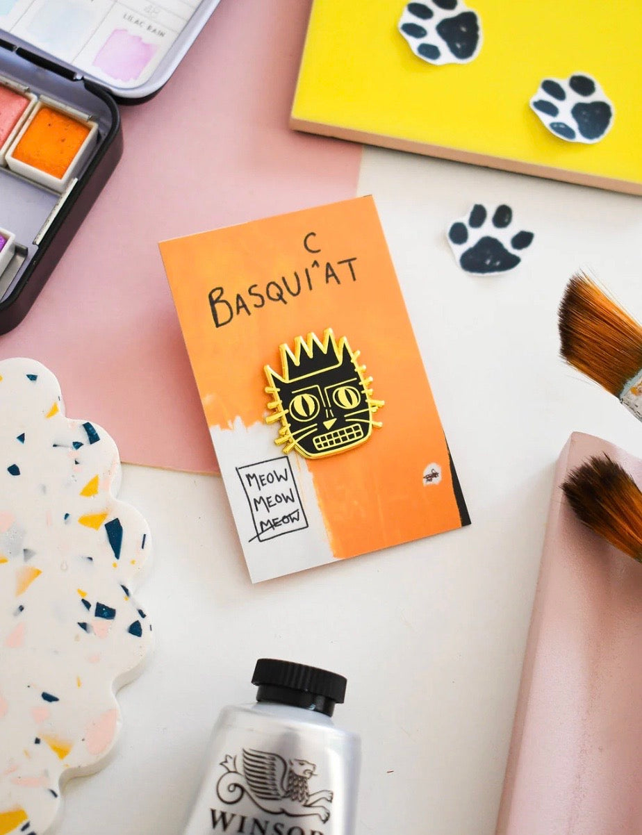 Pin badge of a cat on orange backing card on a desk of art supplies.
