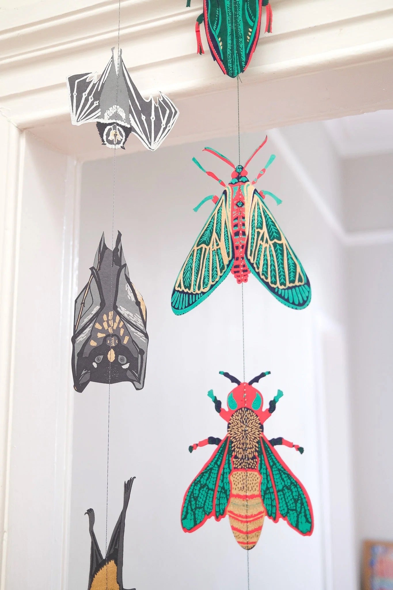 Colourful insect and bat themed decorations hanging on a white wall.