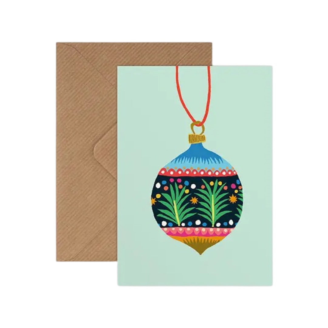 Christmas card with a colourful patterned Christmas bauble on a pale blue background with a brown kraft envelope.