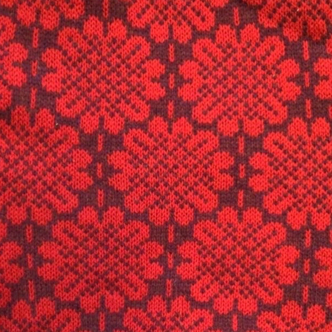A soft and cosy 100% lambswool knitted snood in a red daisy design against a deep red background.