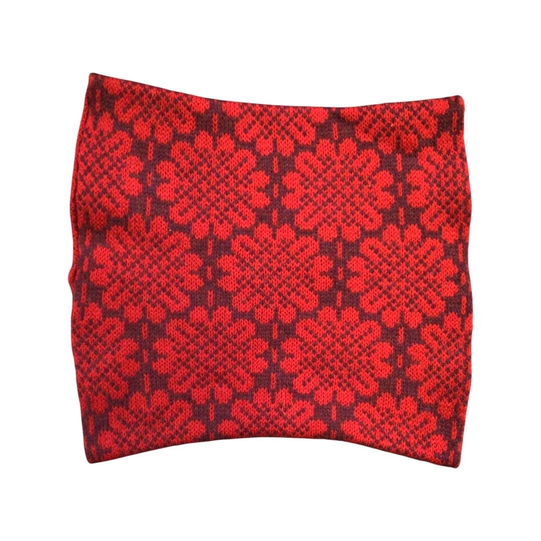 A soft and cosy 100% lambswool knitted snood in a red daisy design against a deep red background.