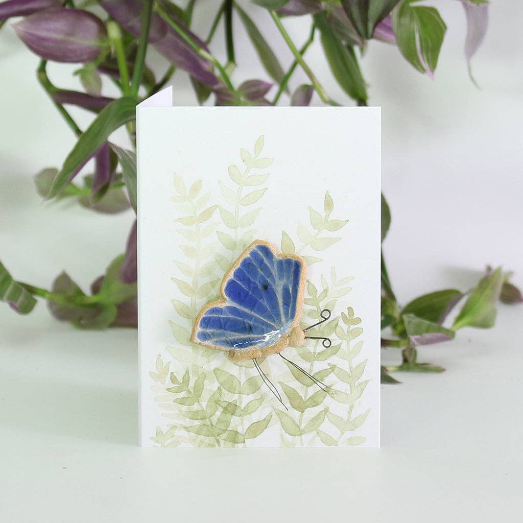 A butterfly shaped ceramic plant hugger with blue recycled glass wings on backing card.