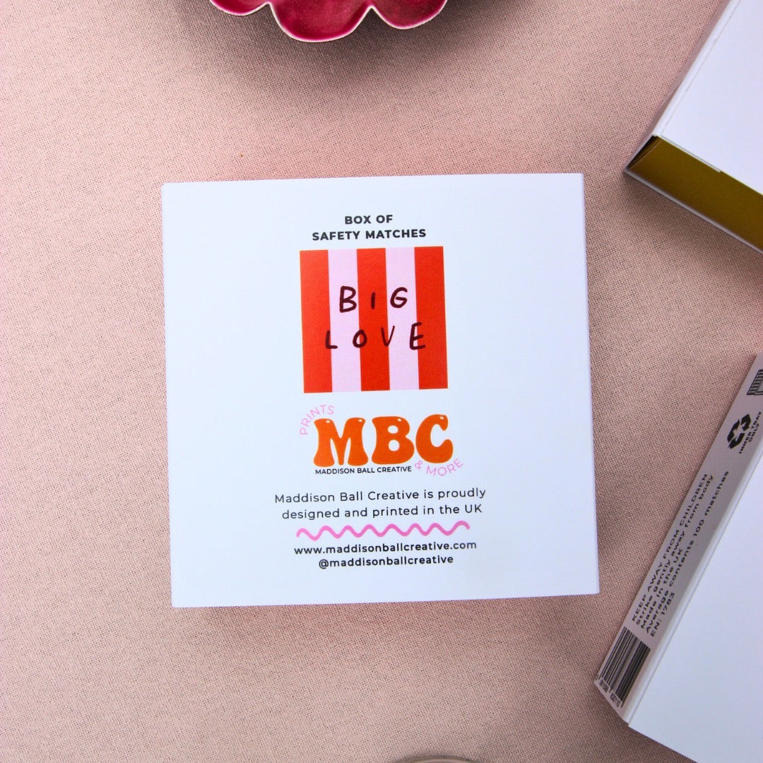 Back of match boxes with a red and pink striped design with the text 'Big Love', on a table. 