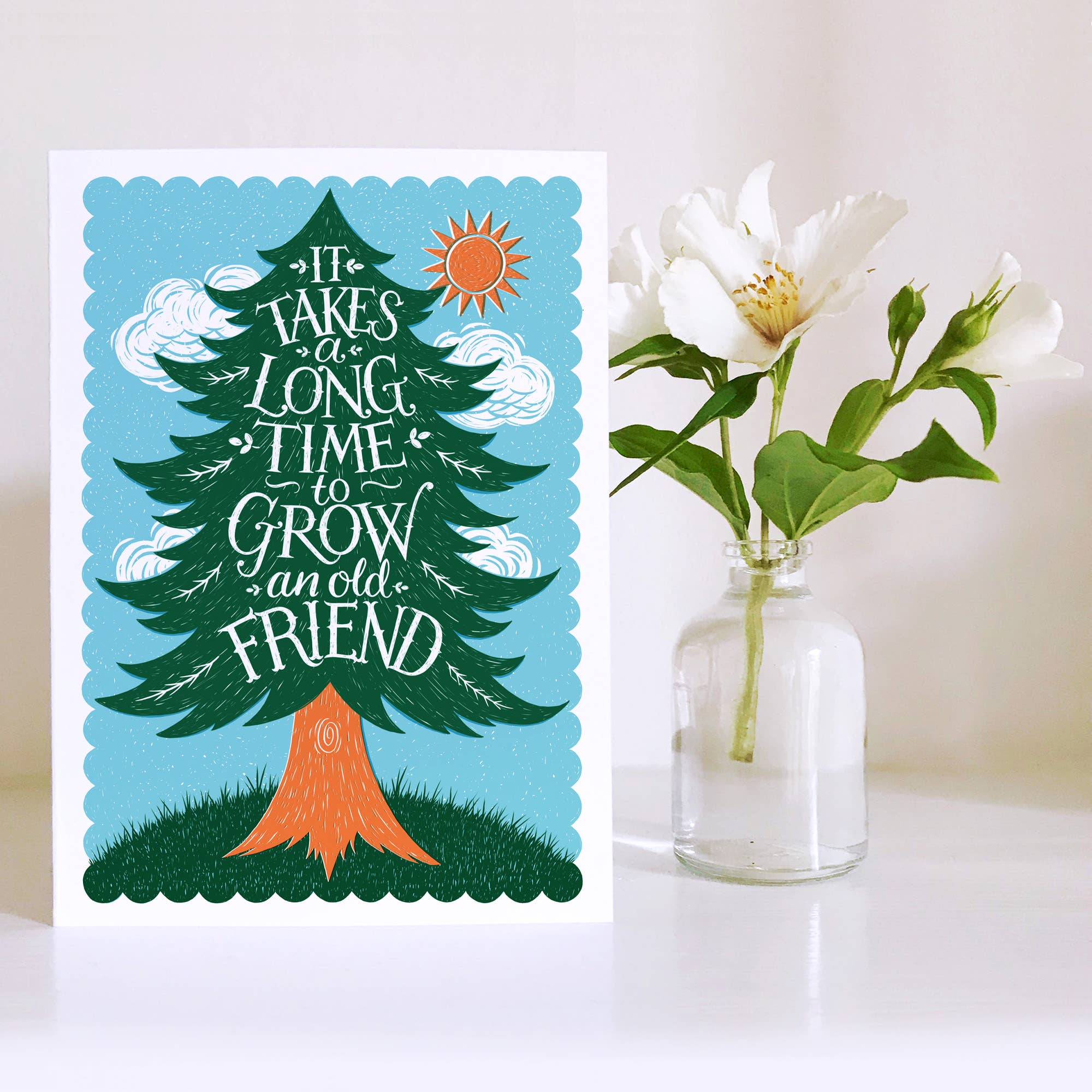 Greeting card with a tree illustration and text 'It takes a long time to grow an old friend' next to a vase with white flowers.