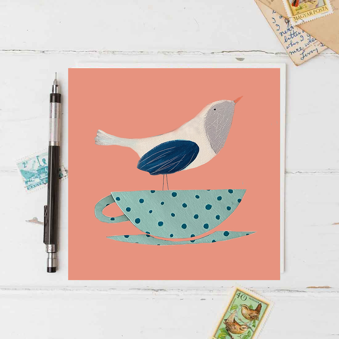 Illustration of a bird on a polka dot teacup with a pen and cards on a white surface.