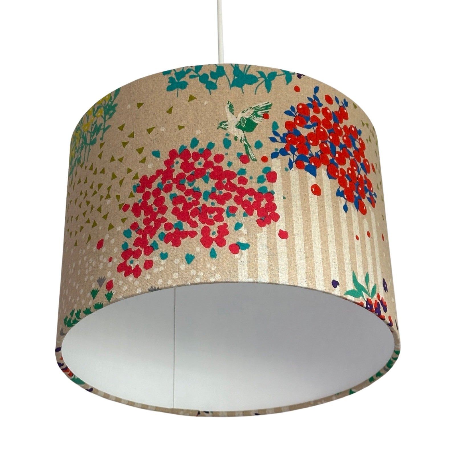 Drum lampshade with colourful clusters of berries and flowers, green and white birds and white stripes on a cream background hanging in a room with a red ceiling and white walls.