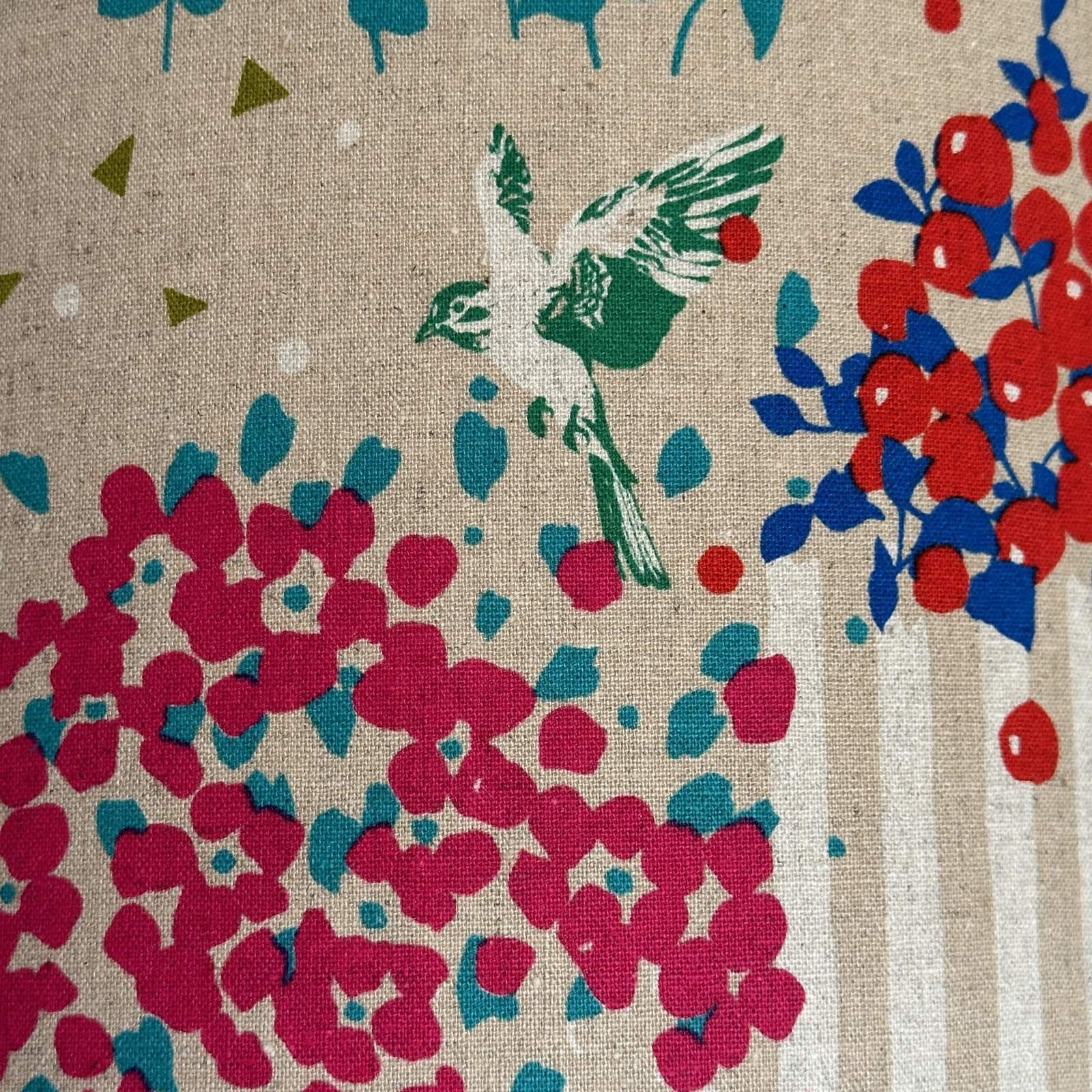 Fabric with colourful clusters of berries and flowers, green and white birds and white stripes on a cream background.