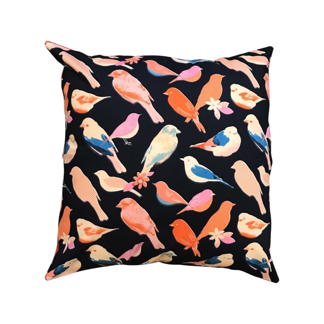 A square cushion cover with a dark background featuring a vibrant pattern of coloured birds in pink, red, and blue.