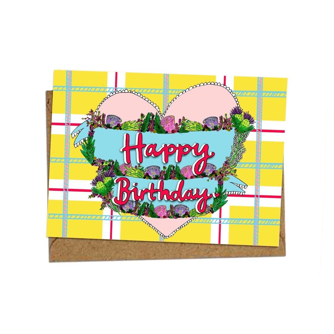 Birthday card featuring the text 'Happy Birthday, written inside a blue banner surrounded by flowers inside a huge pink love heart, all on a yellow tartan background.