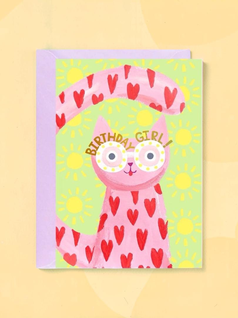 Birthday card with a pink cat illustration and heart patterns on a yellow background.