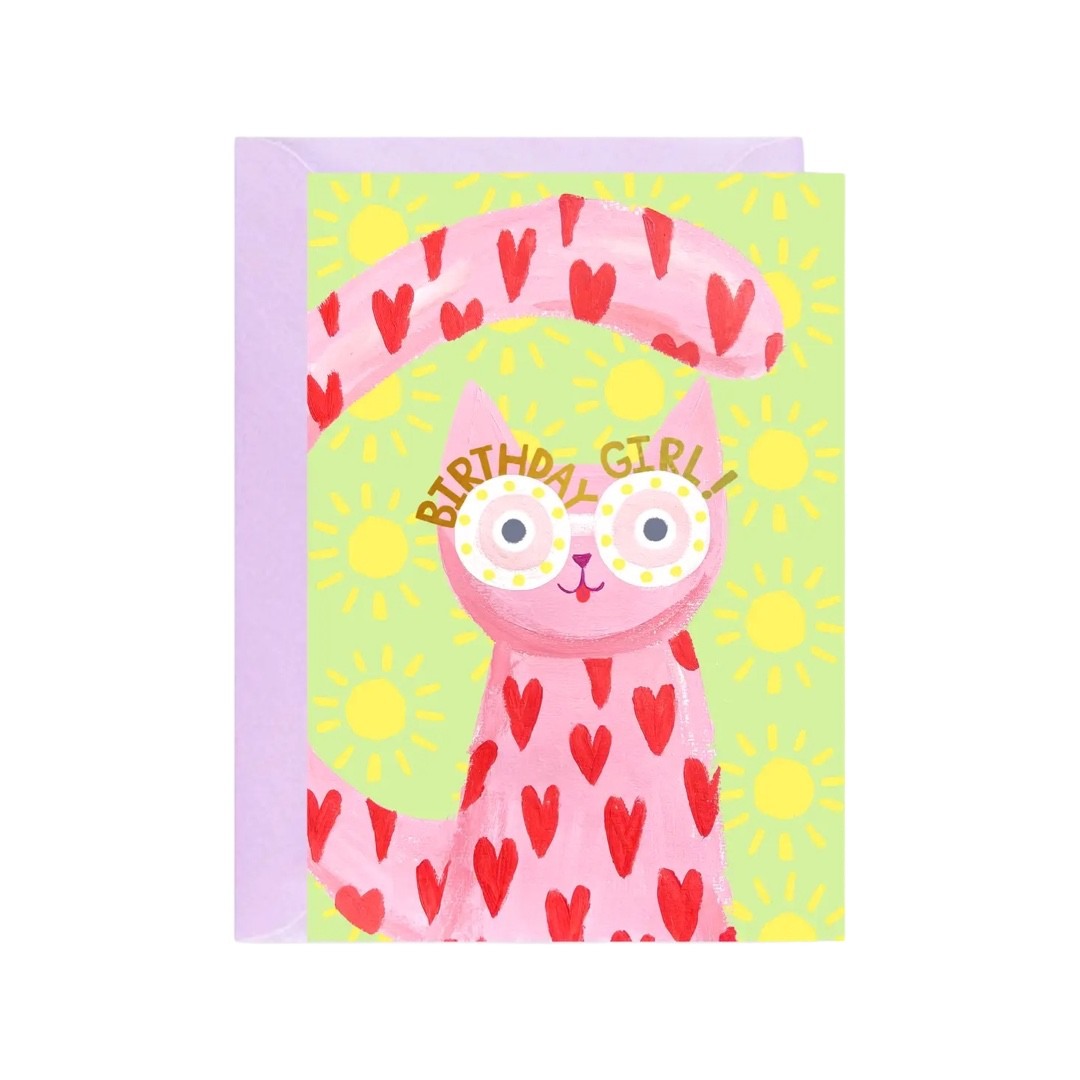Birthday card featuring an illustration of a pink cat with red love hearts and white glasses and the text 'Birthday Girl!' in gold on top of the glasses, all on a light green background with yellow flowers.