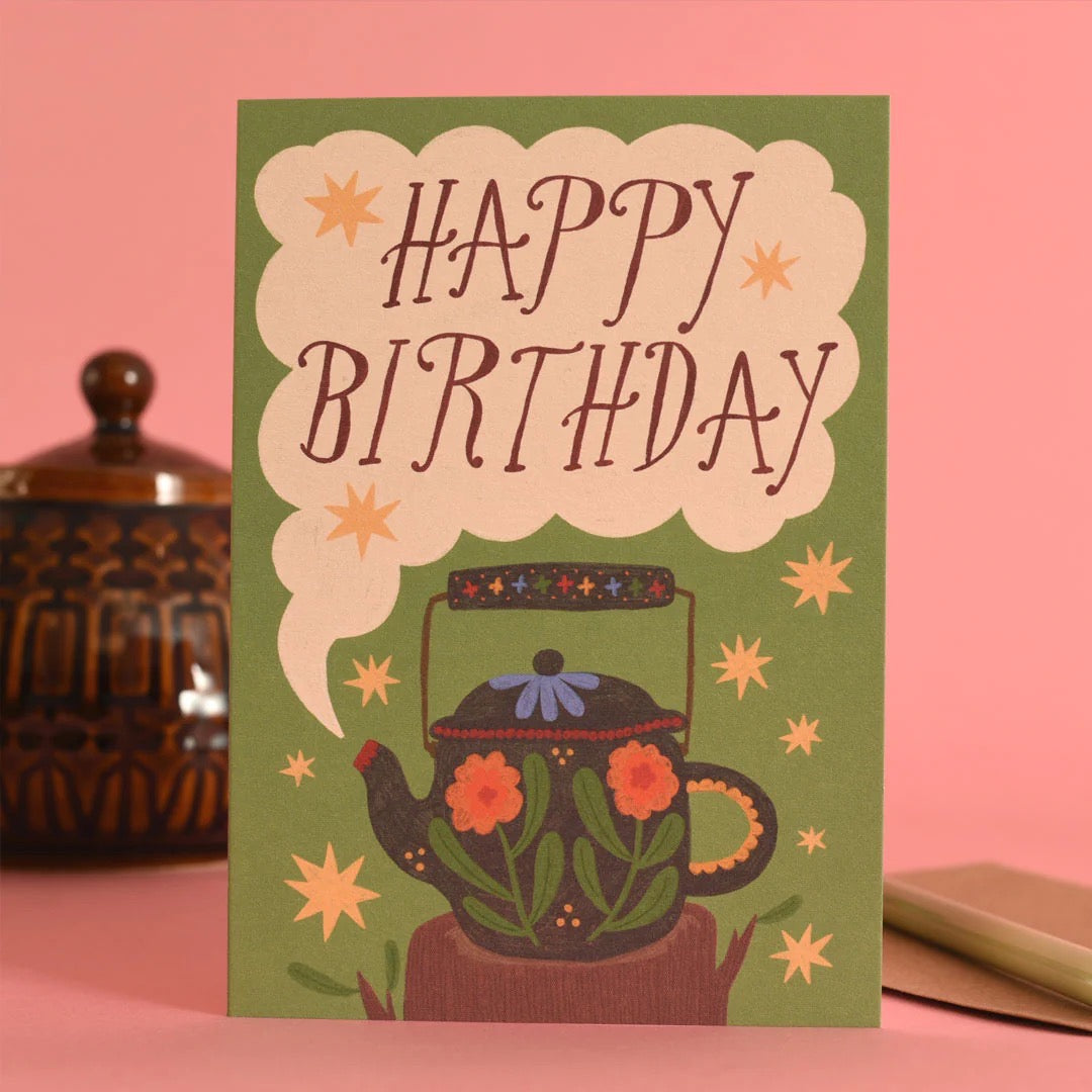 Birthday card with teapot illustration and 'Happy Birthday' text on a pink background.