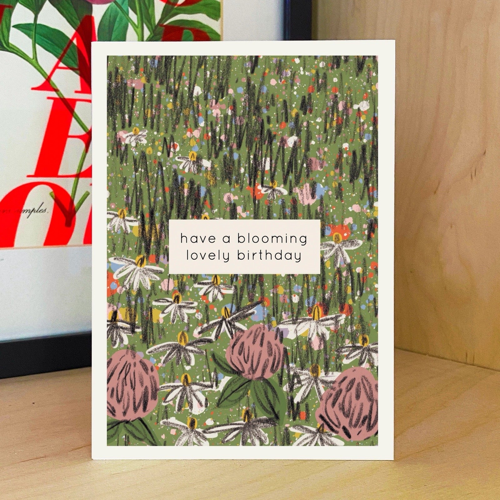 Greeting card with floral design and text 'have a blooming lovely birthday' on a wooden surface.