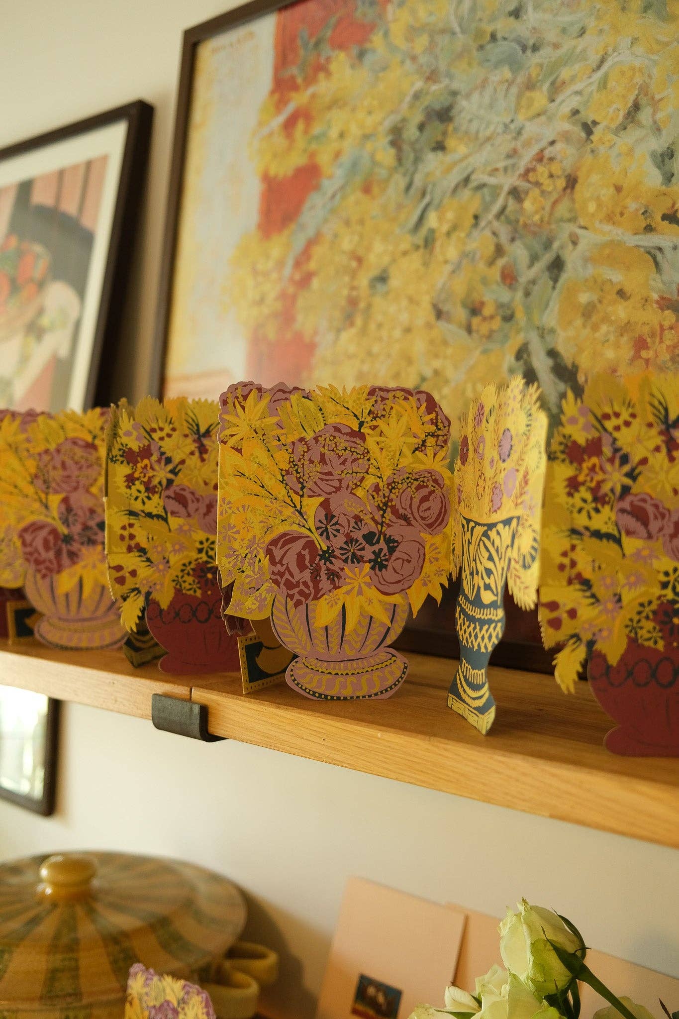 Decorative floral arrangements on a shelf with a colourful painting in the background.